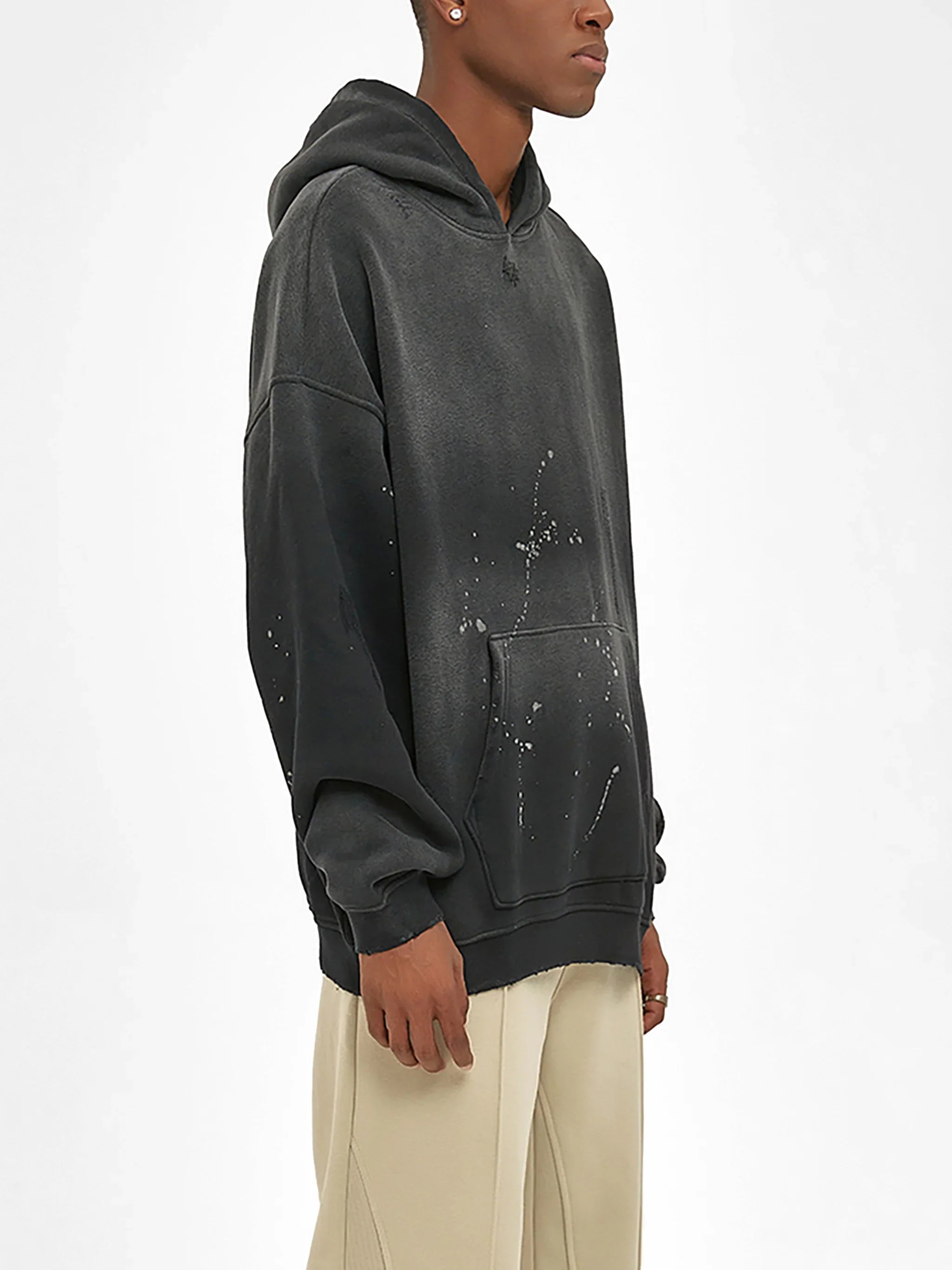 Man wearing a black oversized hoodie with paint splatter details and cream pants